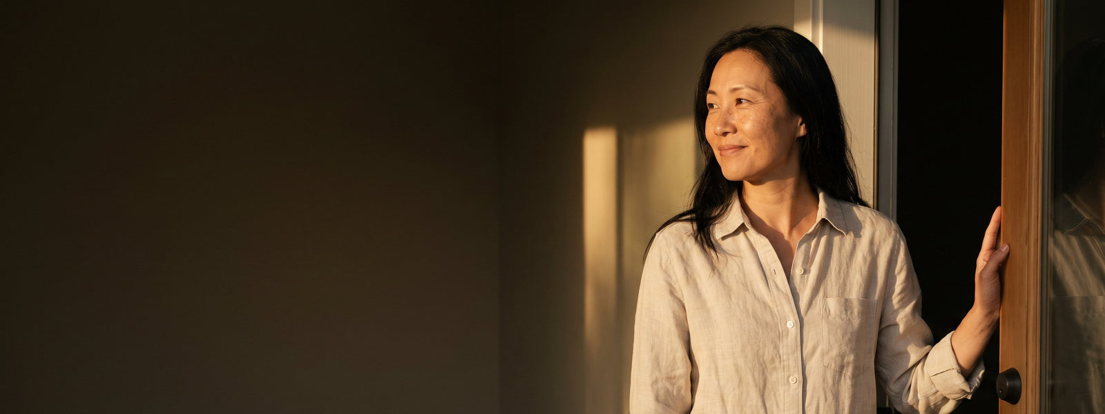A woman at her open front door in the last of the afternoon light, turning back into the house