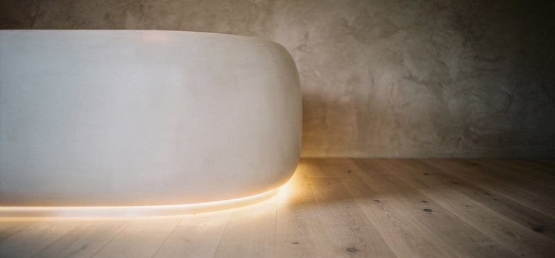 White cylindrical object with a warm glow on a wooden floor against a textured wall.